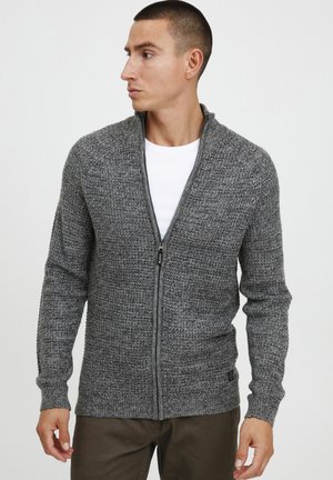 Sivi zip-up kardigan s teksturiranim pletenim dizajnom, rebrastim manžetama i debelim šalom. Nosite ga preko bijele majice.