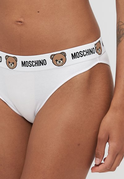 Baltās kokvilnas biksītes ar melnu un brūnu lāča raksta jostu, kurā melnā krāsā izdrukāts zīmola nosaukums "MOSCHINO".