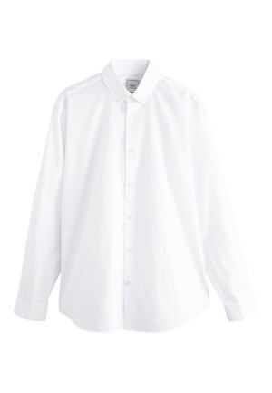 Chemise blanche à boutons associée à un pantalon foncé. La chemise présente un col classique ; le pantalon est cintré avec une texture lisse. Des chaussures noires complètent le look.