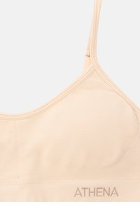 Soutien-gorge de sport seamless pêche clair avec des bretelles réglables, un éclat subtil, et le nom de la marque "ATHENA" affiché dans une teinte douce sur la bande.