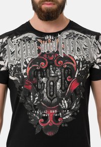 Schwarzes T-Shirt mit einem detaillierten Grafikdesign in Rot- und Silbertönen, floralen Mustern und strukturierten Verzierungen auf der Vorderseite.