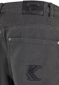 Mørk grå denim bukser med teksturert overflate, med en svart lærmerke og en brodert logo på baklommen.