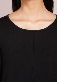 Schwarzer Strickpullover mit rundem Ausschnitt, der über eine gerippte Textur und eine zentrale Nahtdetails verfügt.