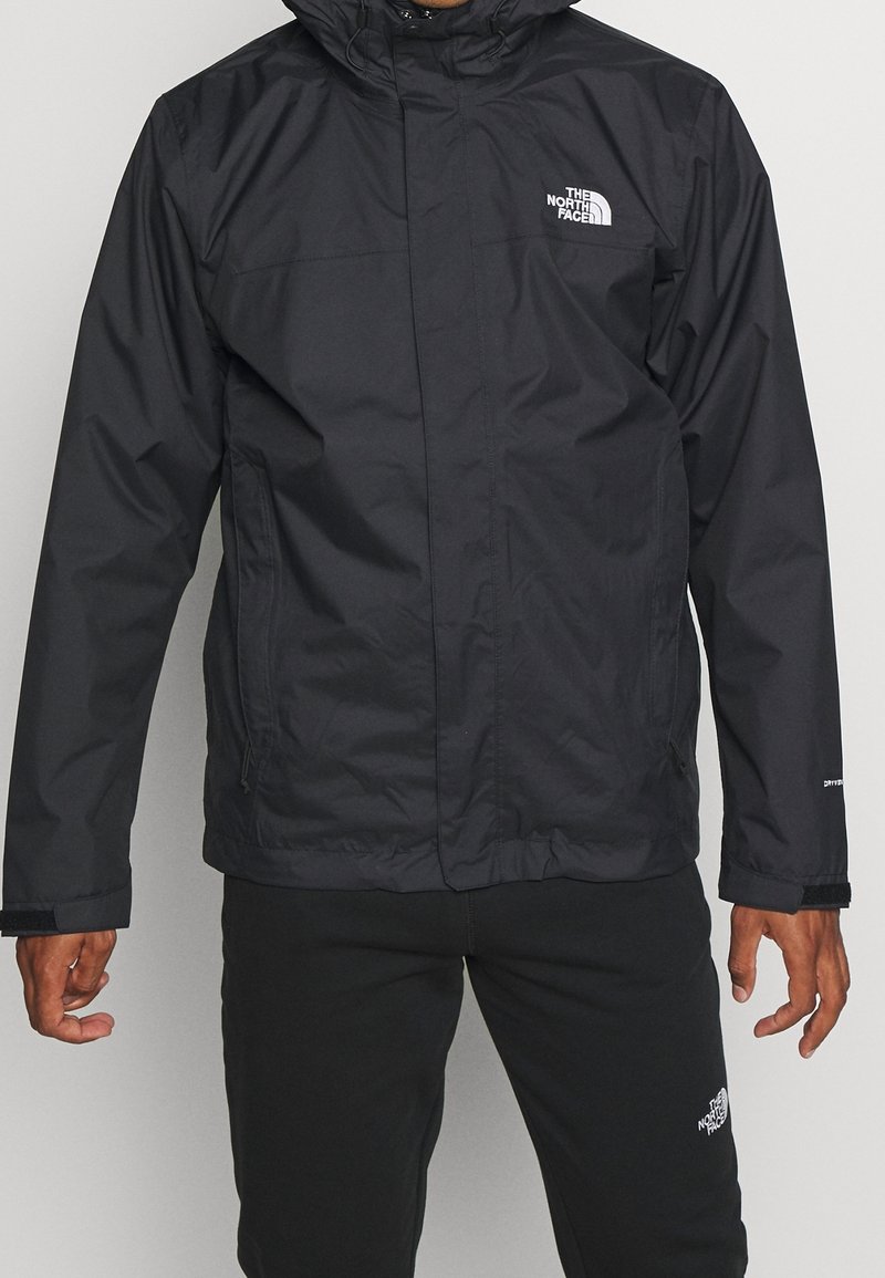 Czarna wodoodporna kurtka z kapturem, zapinana na zamek, z regulowanymi mankietami i logo na lewej piersi. Gładki, lekki materiał.