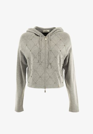Sudadera corta gris hecha de una tela suave, con cremallera en la parte delantera, costuras en patrón de diamante y tachuelas decorativas distribuidas a lo largo.
