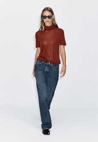 Rust-colored short-sleeve turtleneck top, paired with loose-fitting blue denim jeans and black strappy sandals. Simple, clean design.