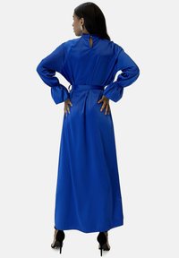 Abito lungo in raso blu con maniche lunghe a sbuffo e vita annodata. Presenta una scollatura a goccia e una silhouette fluente.