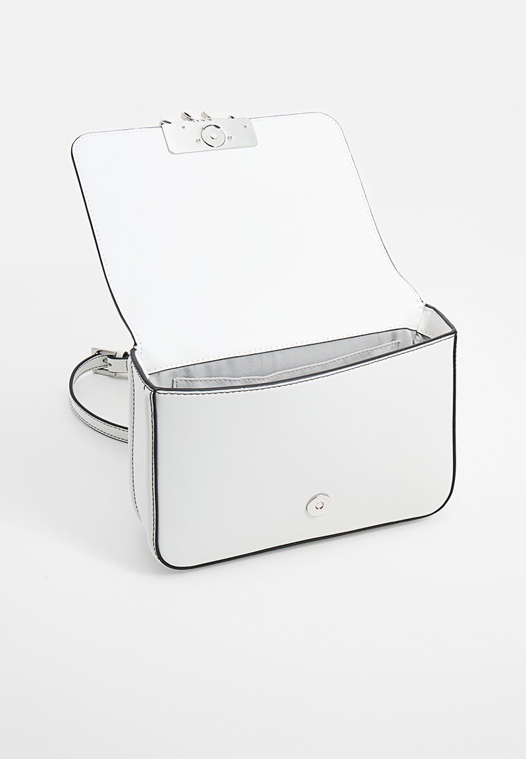 Sac à main en cuir blanc au design structuré, avec des finitions en métal argenté et des bordures noires. S'ouvre pour révéler un intérieur spacieux et gris sans compartiments supplémentaires.