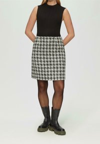 Top sin mangas negro con textura acanalada combinado con falda de pata de gallo blanca y negra, con bolsillos. Se lleva con botines negros de suela gruesa.