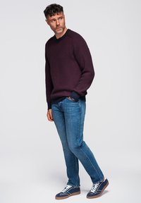 Maroon neule, jossa on tekstuurinen kuvio ja laivastonsiniset ribbireunat, käytetään sinisten farkkujen ja laivastonsinisten tennareiden kanssa, joissa on valkoiset nauhat ja vaaleanruskeat pohjat.