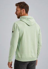 Sudadera verde claro con capucha ajustable, puños y dobladillo de canalé. Presenta un bolsillo con parche en la manga izquierda, material de algodón suave.