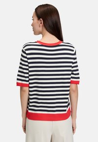 Stribet sweater i marineblå og hvid med røde accenter. Korte ærmer og ribbet kant, med en afslappet pasform og en rund halsudskæring.