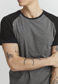  camiseta de manga corta gris y negra con un diseño raglán. Tejido suave y texturizado. Presenta un escote negro y mangas en contraste.
