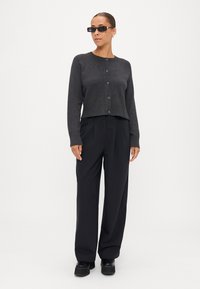 Mörkgrå kort cardigan med knappstängning, ribbad nederkant och långa ärmar, i kombination med svarta vida byxor och kraftiga svarta loafers.