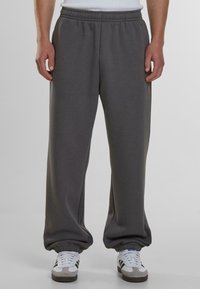 Pantalones de chándal grises con corte relajado, cintura elástica y puños acanalados, fabricados con un tejido suave. Combinados con zapatillas blancas.