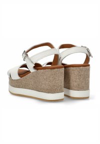 Sandalias de cuña de cuero blanco con punta abierta, que cuentan con un tacón de tela marrón texturizada, correa ajustable y suela de goma beige.