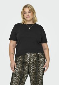 T-shirt preta de algodão com mangas curtas, combinada com calças de padrão leopardo com uma textura brilhante e um detalhe de fivela prateada.