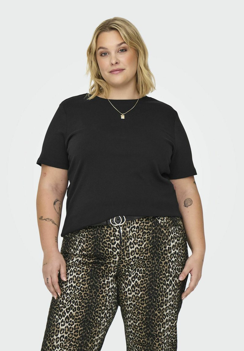 T-shirt preta de algodão com mangas curtas, combinada com calças de padrão leopardo com uma textura brilhante e um detalhe de fivela prateada.