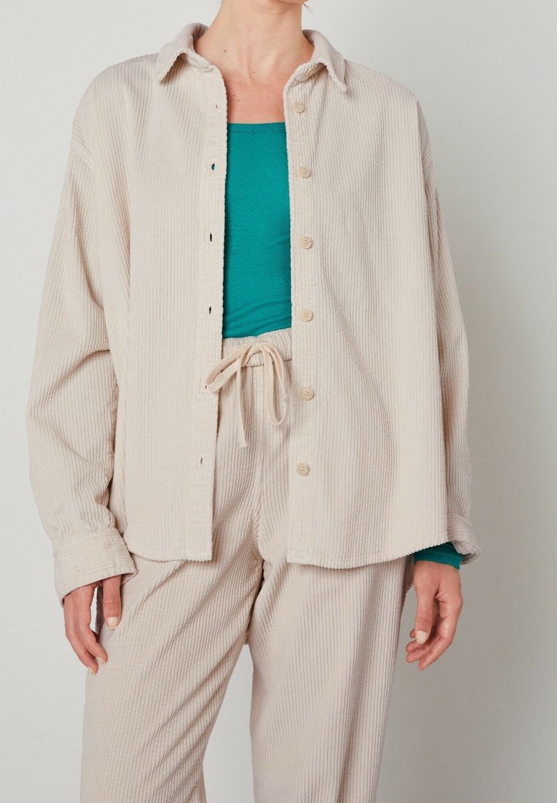 Beige corduroy overshirt with button closure and a collar, paired with a teal fitted top and matching beige corduroy pants.