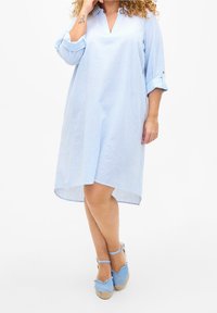 Helles blau gestreiftes Hemdkleid mit Kragen, Dreiviertelarmen und einem leicht längeren Rückenteil. Kombiniert mit blauen Espadrilles.