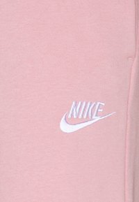 Pink Nike sweatpants made from soft fabric featuring an embroidered white logo on the left side. Smooth texture with a casual design.
