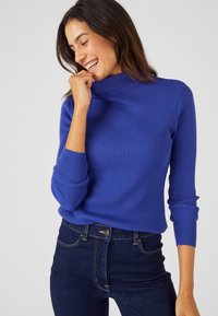 Maglione a collo alto a coste di un blu vibrante, con maniche lunghe e design aderente, abbinato a jeans blu scuro.
