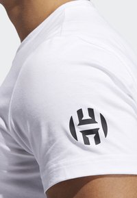 Camiseta de algodón blanca con un logo negro en la manga izquierda. La tela es suave, tiene mangas cortas y un diseño de cuello redondo.