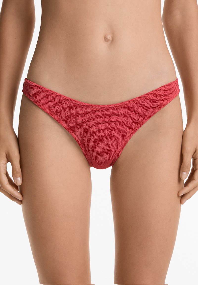 Slip in bikini rosso con un design tessuto testurizzato. Spalline sottili ai lati e copertura moderata nella parte posteriore. Finitura in tessuto morbido.