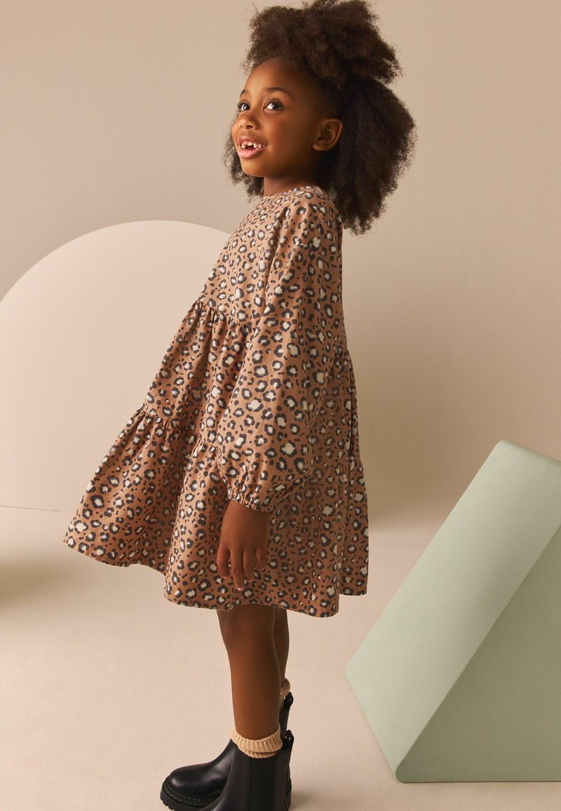 Leopardenmuster Kleid mit langen, gepufften Ärmeln und einem gestuften Rock. Der Stoff ist weich, in braun- und schwarzen Tönen, kombiniert mit schwarzen Stiefeln.