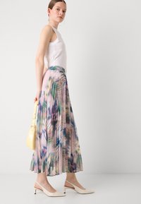 Gonna maxi plissettata in un pattern floreale multicolore, con una vita sottile, abbinata a una canotta bianca e a delle décolleté crema con cinturino.