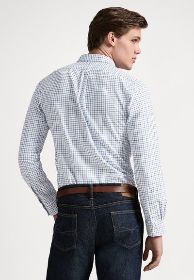 Λευκό πουκάμισο με κουμπιά και μπλε σχέδιο σε δίκτυο, συνδυασμένο με σκούρο τζιν και καφέ δερμάτινη ζώνη. Διαθέτει μακριά μανίκια και κλασικό γιακά.