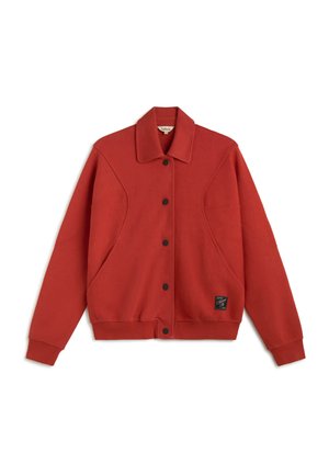 Chaqueta roja de manga larga con botones a presión negros, cuello, bolsillos laterales y un pequeño parche con logo negro cerca del dobladillo inferior en la parte delantera.