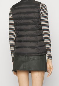 Gilet imbottito nero con design a righe orizzontali, indossato sopra una camicia a maniche lunghe multicolore a righe, abbinato a una mini gonna di jeans nera.