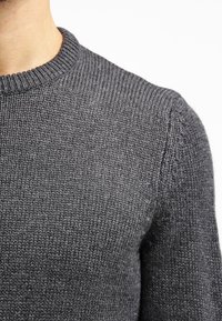 Szary dzianinowy sweter z okrągłym dekoltem, wyróżniający się teksturowanym materiałem i ściągaczami na mankietach. Zbliżenie ukazuje delikatne detale przeszyć oraz gładkie wykończenie.