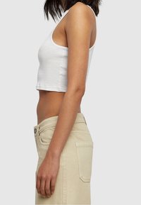 Top court blanc en tissu côtelé associé à un jean taille haute beige clair. Mettez l'accent sur le design simple et la forme ajustée de la tenue.