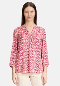 Bedruckte Bluse in pink, weiß und lila mit wirbelndem Muster; lockere Passform mit langen Ärmeln und V-Ausschnitt; weicher Stofftextur.