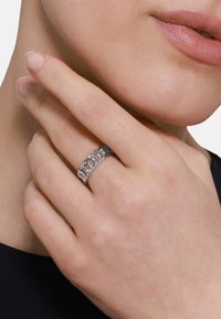 Anello in argento a maglia con una superficie texturizzata e un design ad incastro, indossato su una mano. È visibile il tono della pelle, con un aspetto naturale delle unghie.