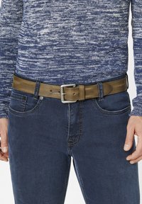 Brauner strukturierten Leder Gürtel mit einer silbernen Metallschnalle, getragen über dunkelblauen Jeans und einem blauen Strickpullover.