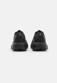 Para czarnych butów biegowych Adidas pokazana z tyłu na białym tle, z grubymi podeszwami i logo na piętach.