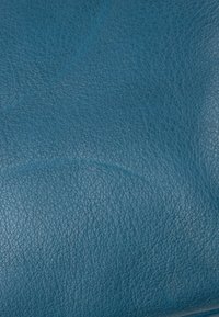 Gros plan d'une surface en cuir bleu texturé montrant un grain fin et des plis naturels.