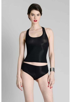 Femme aux cheveux courts et foncés portant un haut noir sans manches et un short, rouge à lèvres et vernis à ongles rouges, avec un bracelet manchette en argent sur fond gris.