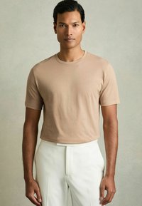 Tricou din bumbac bej cu guler rotund și mâneci scurte, asortat cu pantaloni albi; textură netedă, design ajustat.