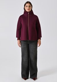 Bordeaux ritsjack met een hoge, geribbelde kraag en losse pasvorm, gecombineerd met wijde zwarte denim jeans en spitse bordeaux hakken.