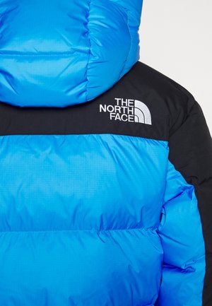 Blauw-zwarte donsjas met capuchon, met wit "The North Face" logo op de rechterbovenrug.