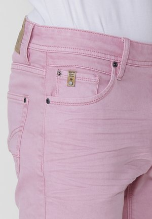 Jeans de mezclilla rosa con cinco bolsillos, featuring etiqueta de marca dorada y herrajes plateados. La tela tiene una textura suave con un ligero desgaste.