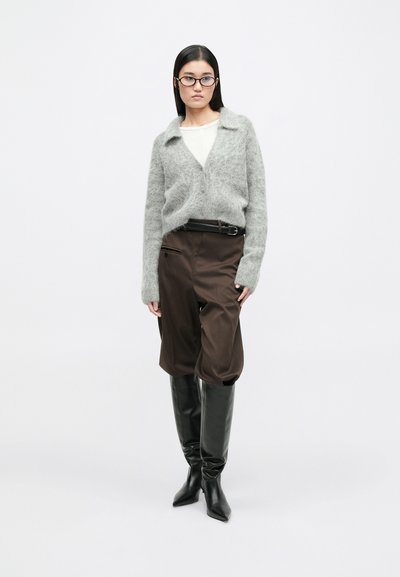 Grijze mohair cardigan, wit topje, bruine broek met wijde pijpen, zwarte riem en zwarte kniehoge laarzen met spitsen en een gestroomlijnd ontwerp.