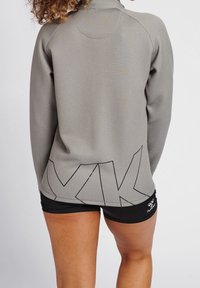 Grå atletisk pullover med hög krage, med textilstruktur, vinklad svart grafisk design vid nederkanten och figurnära siluett.