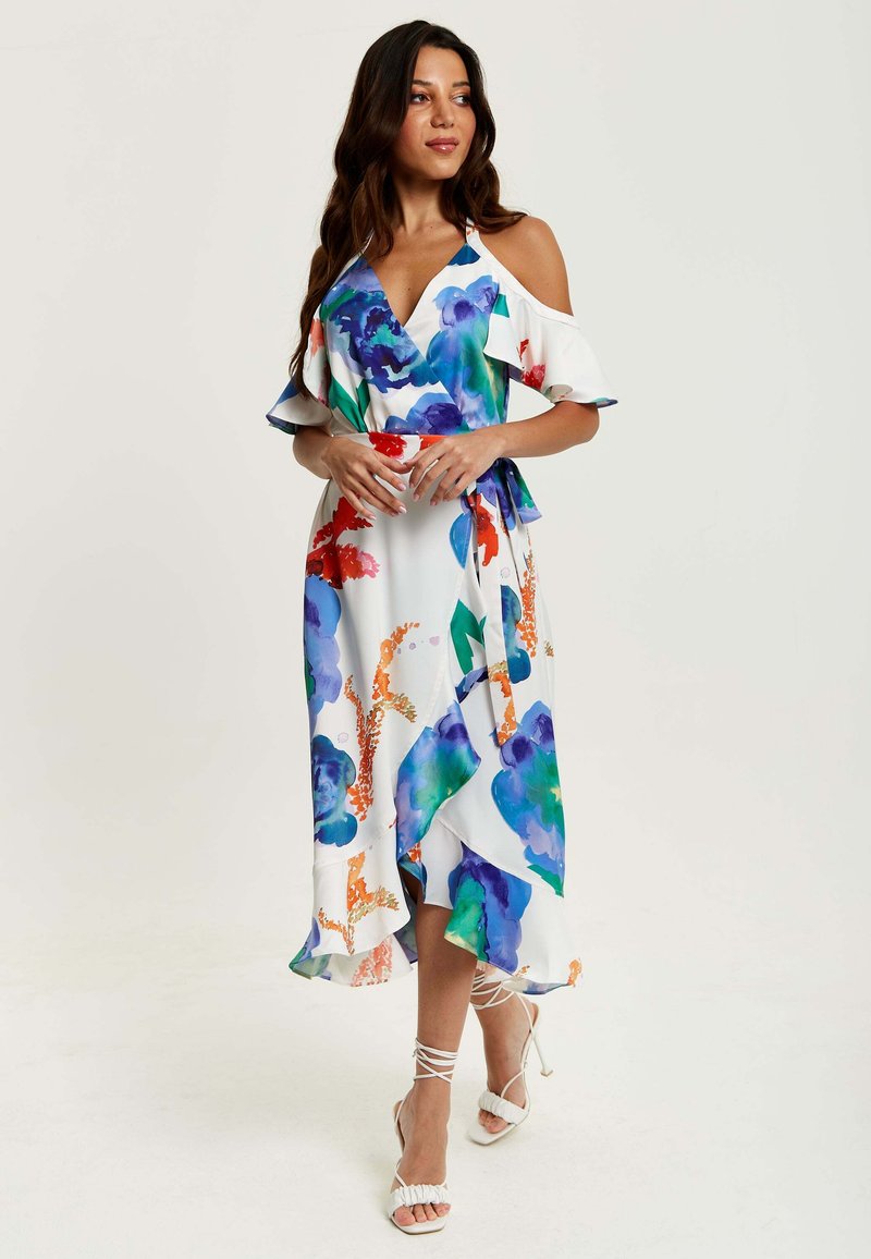 Floral wrap dress in white with blue, red, and green patterns. Features cold shoulder sleeves, a tie waist, and a ruffled hem.