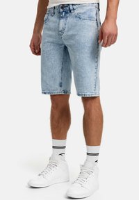 Pantaloni scurți de denim albastru deschis cu croială dreaptă, cu buzunare în spate și tiv brut, asortați cu adidași albi înalți și șosete cu dungi.