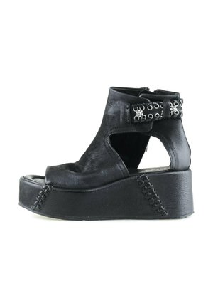 Sandalo platform in pelle nera con punta aperta, lati ritagliati, cinturino alla caviglia con occhielli e borchie argentate, e suola spessa cucita.